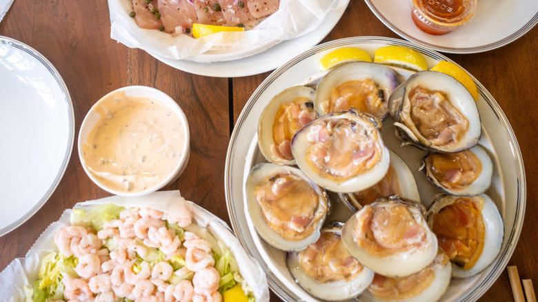 Assorted seafood on plates on a wood table, with a platter of shrimp, a bowl of remoulade, and a plate with open-shelled shucked oysters