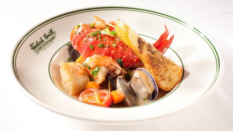 White dish rimmed in green with "Tadich Grill" written in cursive on the left-hand side, loaded with lobster, filet of fish, open mussels, and other seafood