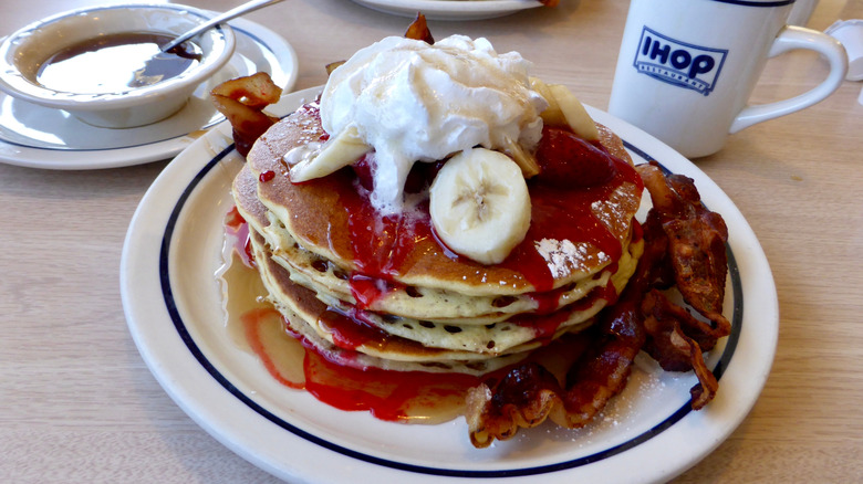 A stack of IHOP pancakes with bacon, bananas, and whipped cream