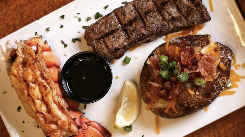 Sizzler steak, lobster tail, and baked potato on a plate
