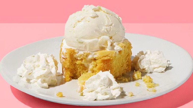 California Pizza Kitchen's Butter Cake sits on a white plate with a scoop of vanilla ice cream on top and three mounds of whipped cream spread throughout the plate