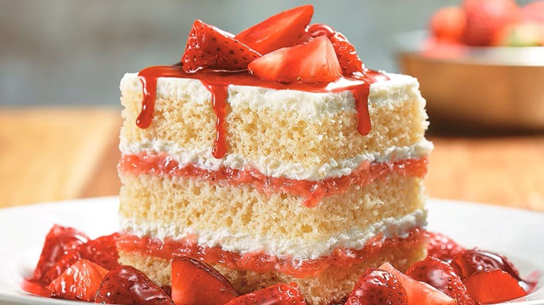LongHorn Steakhouse's Strawberries & Cream Shortcake sits on a white plate with sliced strawberries surrounding the cake