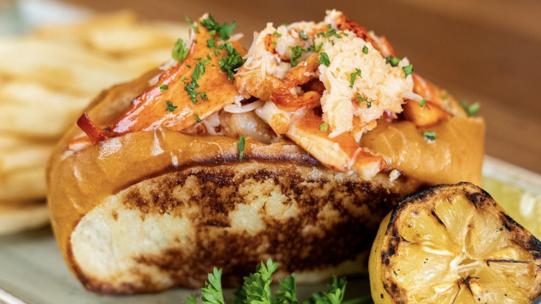 Bluewater Grill lobster roll sitting on a plate with two pickle slices and a small bowl of melted butter.