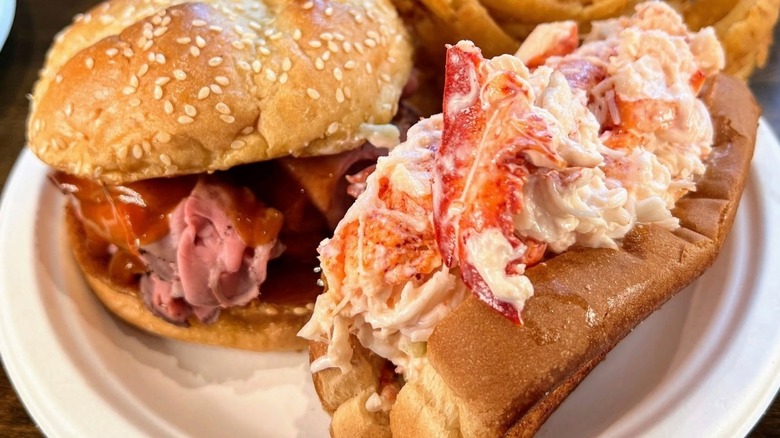 Roast beef sandwich with barbecue sauce next to an overstuffed lobster roll on a plate with onion rings from Kelly's Roast Beef.