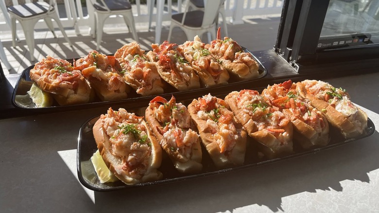 Two plates of six lobster rolls each from Quincy's Original Lobster Rolls on a table next to a patio.