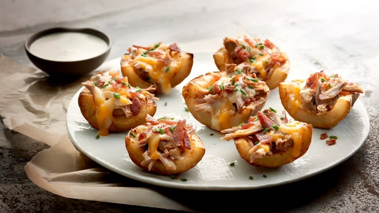 Potato skins with cheese, chicken, and bacon on plate with sour cream dip in background