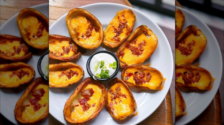 Plate of cheesy potato skins with cup of sour cream