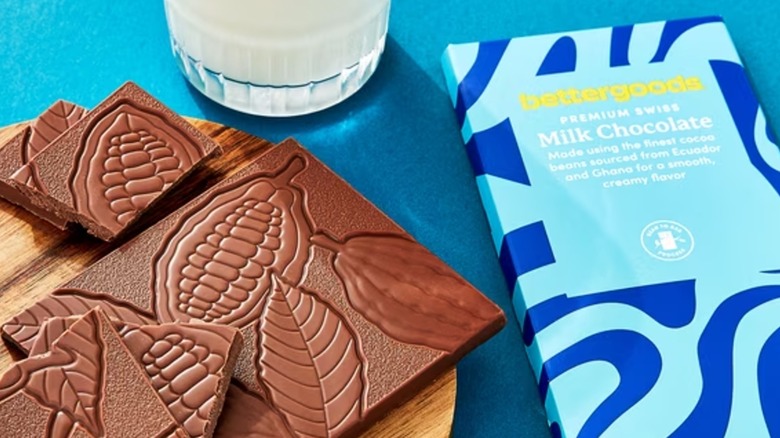 Several pieces of chocolate bar alongside wrapper and glass of milk