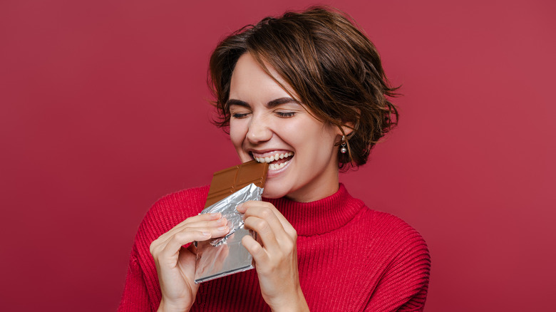 Woman biting into chocolate bar wrapped in foil