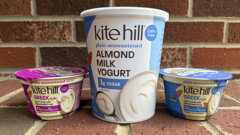 Three flavors of Kite Hill plant-based yogurt lined up on brick surface, two small and one large