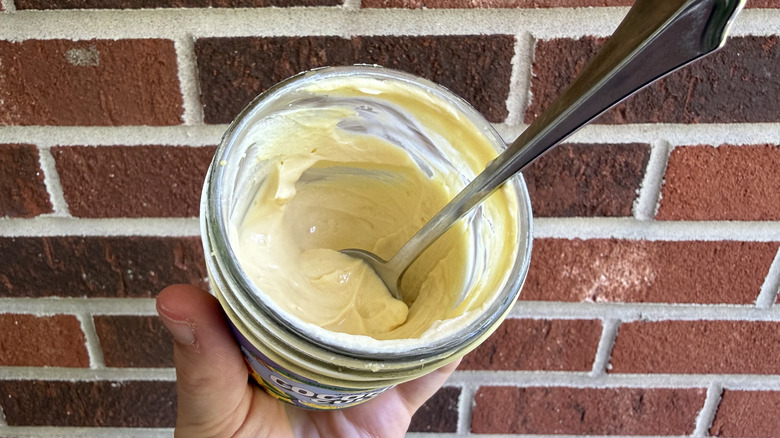 Hand holding open glass jar of Coconut Cult yogurt with spoon