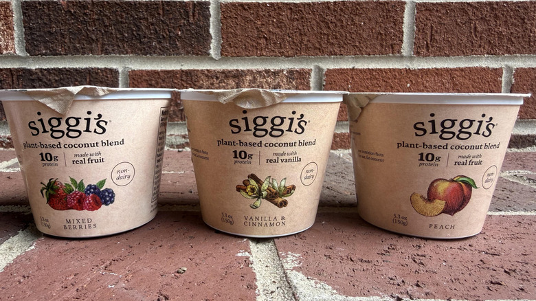 Three flavors of Siggi's plant-based yogurt lined up on brick surface