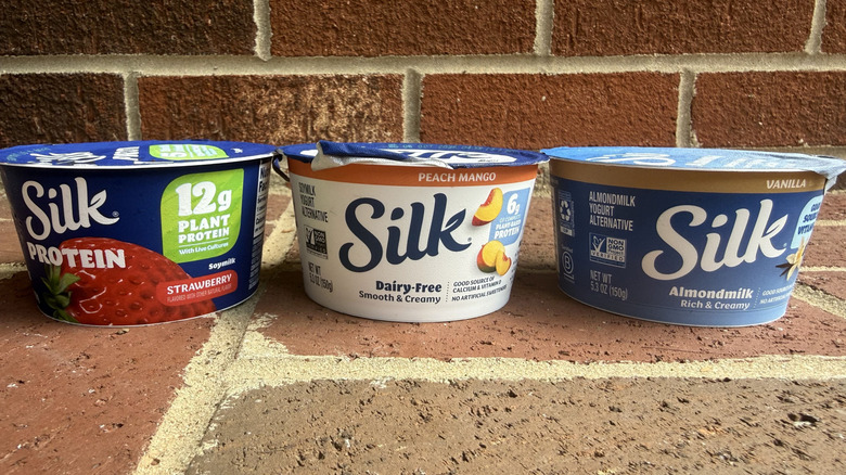 Three flavors of Silk dairy-free yogurt lined up on brick surface