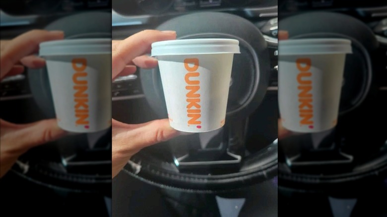 Hand holding tiny cup of Dunkin' espresso in car