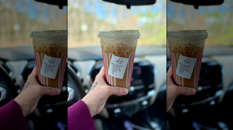 Hand holding Dunkin' iced cappuccino in car