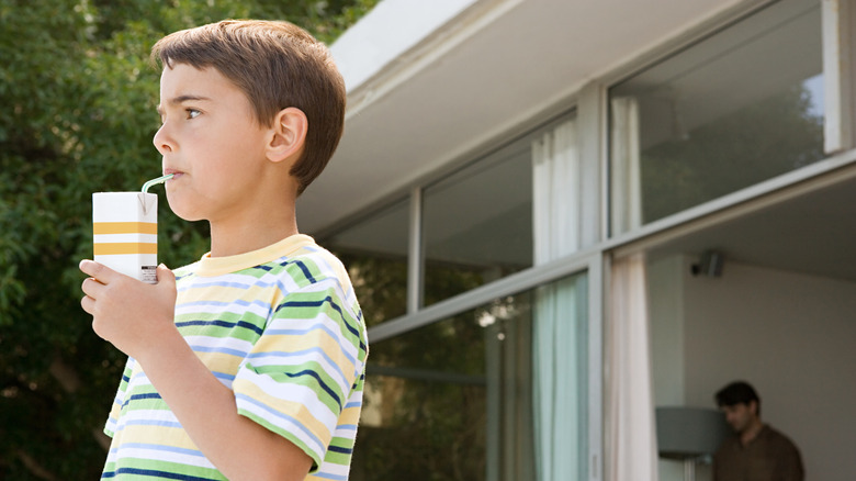 Little boy in t-shirt outside drinking from juice box