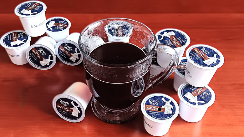 Dutch Bros mafia dark roast coffee pods on table next to glass mug of black coffee.