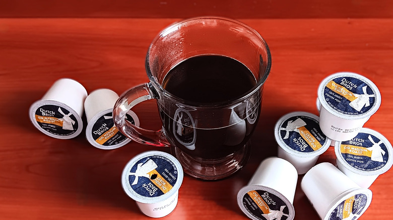 Dutch Bros OG medium roast coffee pods on table next to glass mug of coffee.