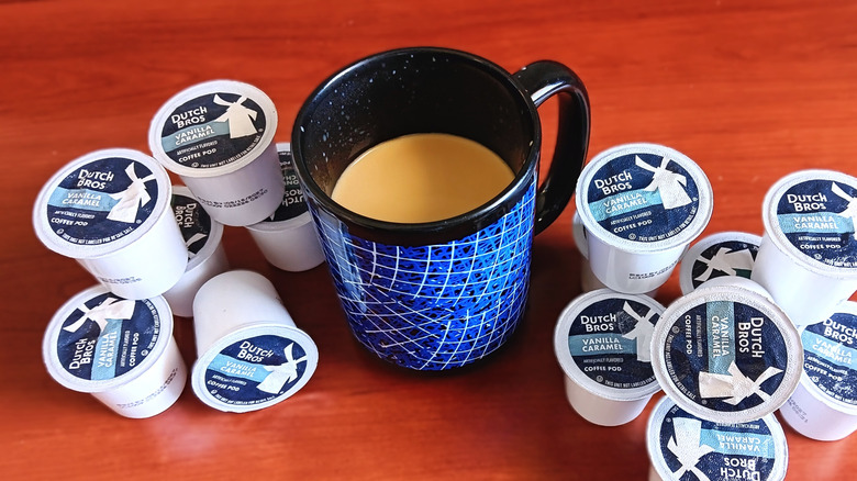 Dutch Bros vanilla caramel coffee pods piled on table near black and blue mug with coffee and cream.