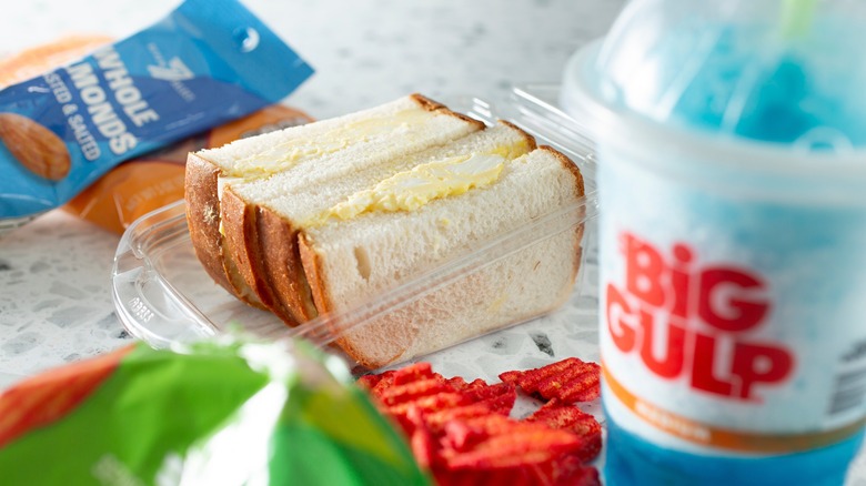 An egg salad sandwich in a plastic container between a bag of 7-Eleven brand almonds and a Big Gulp