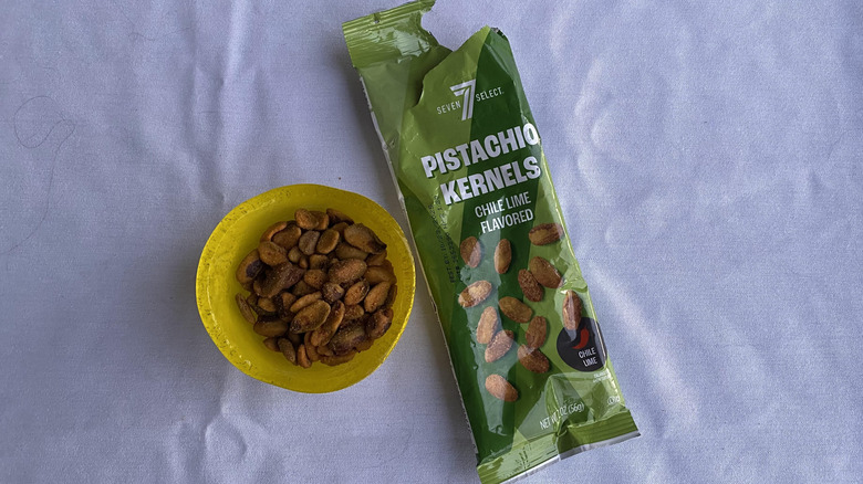 Seasoned pistachios in yellow dish by green plastic bag