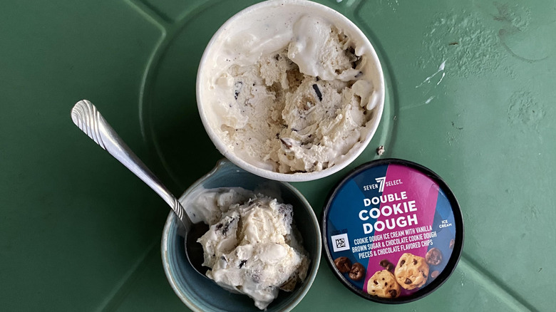 Cookie dough ice cream container opened and spoon in blue bowl of ice cream