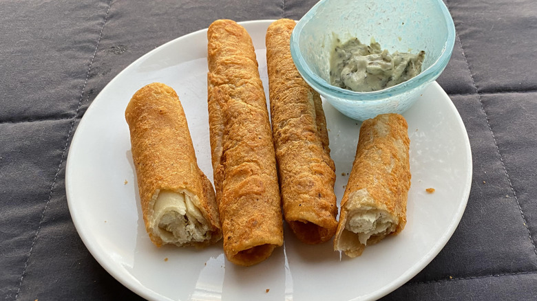 Crispy golden taquitos on white plate with dipping sauce