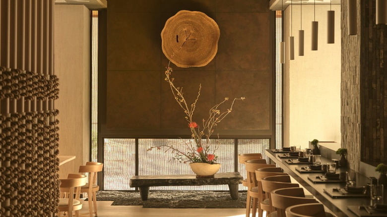 the inside of a beige restaurant with a big plant and lights hanging