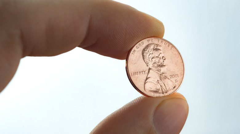 Fingers holding a single penny