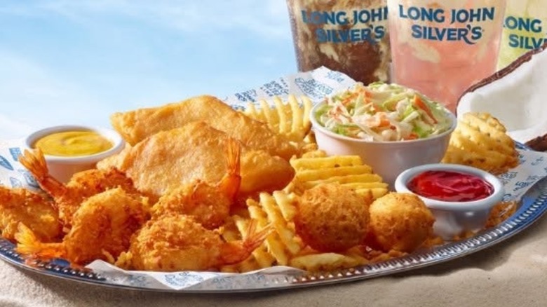 Platter of fish, fries, hush puppies, and sides with three drinks in background