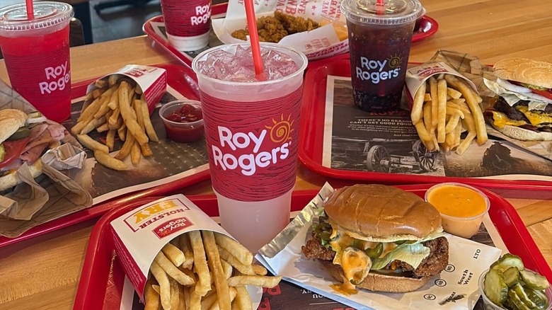 Four trays of food with burgers, fries, and drinks