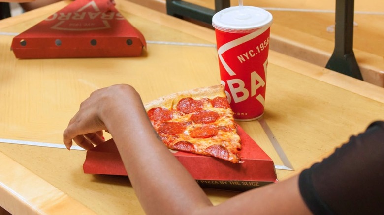 Over the shoulder of table with slice of pizza, boxes, and Sbarro's soda