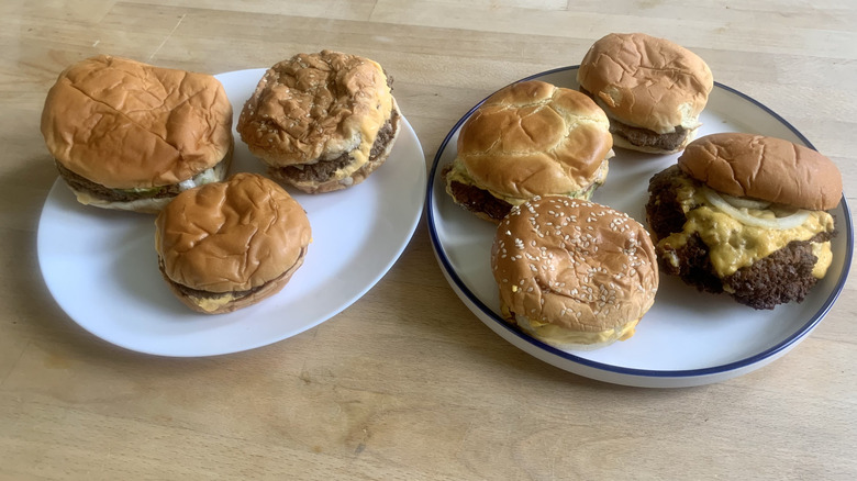 seven double cheeseburgers on two plates on wood table