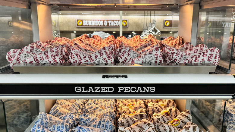 Rows of glazed pecans and other glazed nuts in paper cones inside a display case at Buc-ee's.