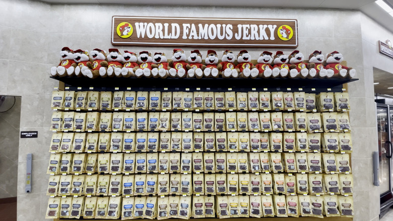 A wall with several rows of jerky in beige-colored bags hanging off of it. A sign above reads "World Famous Jerky," while a line of plushies depicting Buc-ee's beaver mascot sits atop the display.