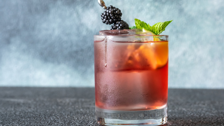 A cocktail glass with blackberries and mint