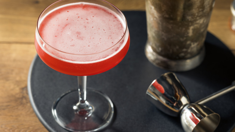 A pink cocktail next to a metal cup