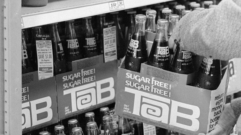 Black and white image of hand removing Tab bottles from store shelf