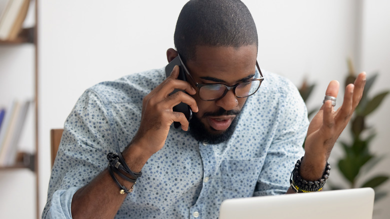 An angry man talking on a cellphone looking at a laptop
