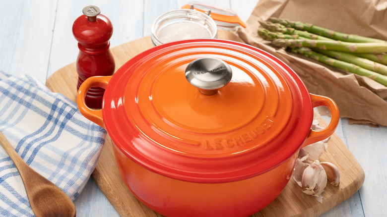 Le Creuset Dutch oven on wooden chopping board with pepper, asparagus and garlic