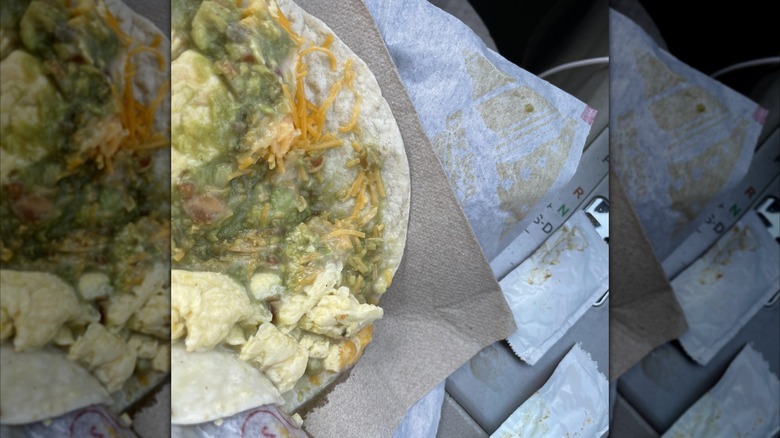 A close up of a breakfast taco with a soggy filling on packaging, mirrored image