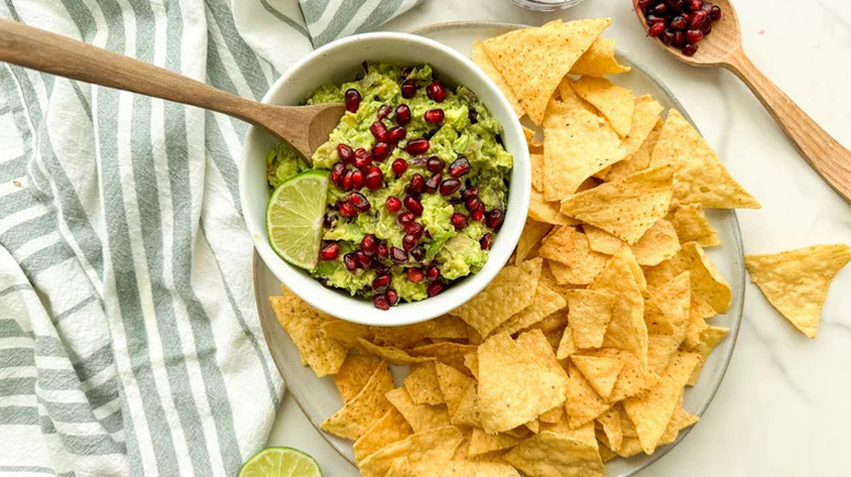 Top view of a colorful pomegranate guacamole in white bowl on plate of chips