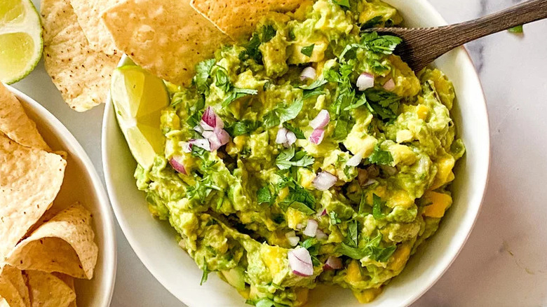 Top view of a fresh mango guacamole in white bowl with lime and chips
