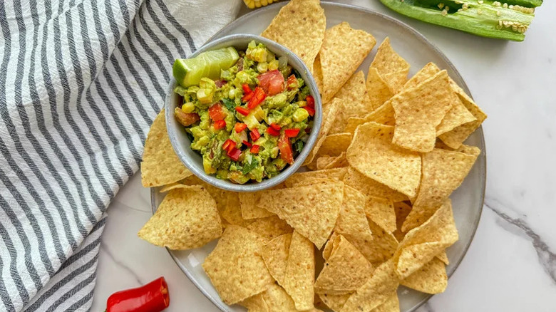 Grilled corn and avocado guacamole in white bowl on plate of chips