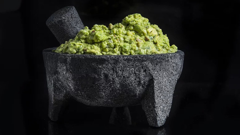 Guacamole with roasted Poblano and pecan in molcajete on black background