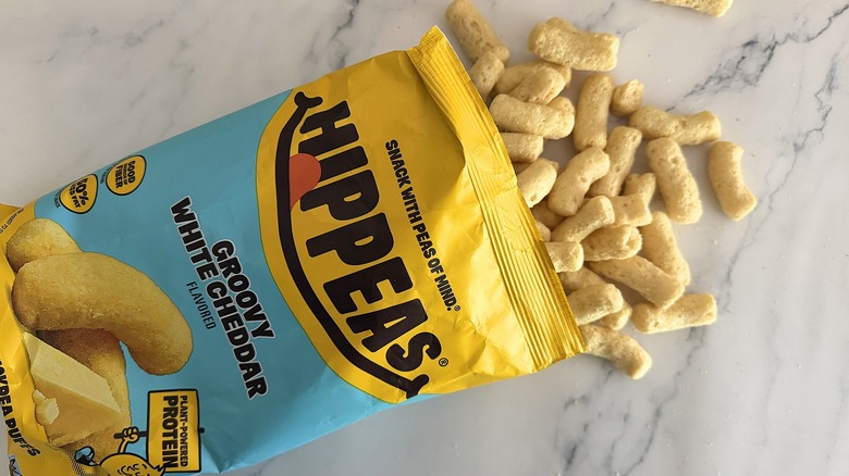 Hippeas spilling out of bag of Groovy White Cheddar Hippeas on white marble surface