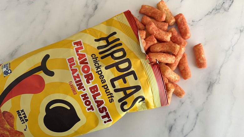Hippeas spilling out of bag of Flavor Blast Blazin' Hot Hippeas on white marble surface