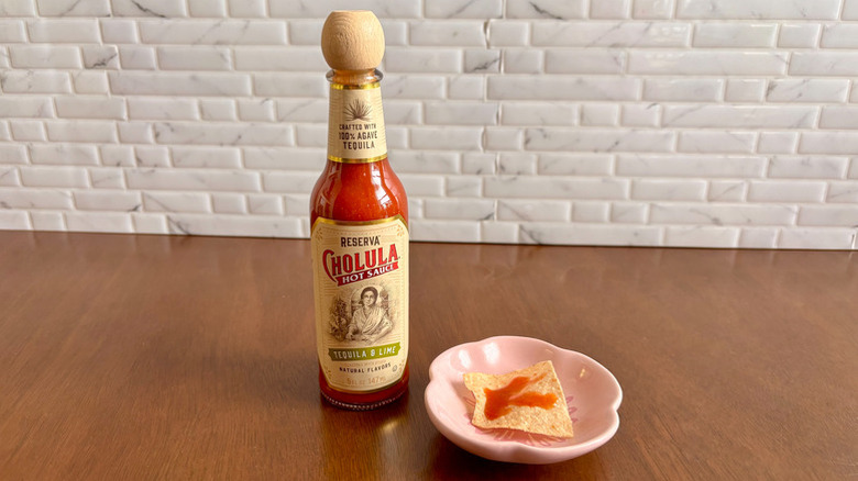 bottle of Cholula Reserva Tequila & Lime hot sauce next to a chip with a dab of sauce on it
