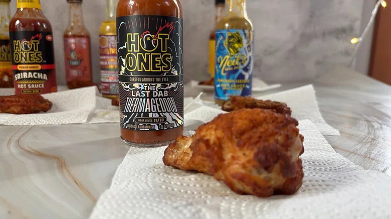 bottle of Hot Ones The Last Dab Thermageddon hot sauce behind a chicken wing on a paper towel with other hot sauce bottles in the background