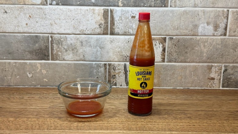 bottle of Louisiana Brand Hotter Flavor hot sauce next to a small bowl with some hot sauce in it
